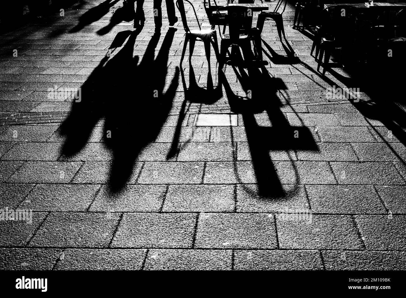 Long shadows of chairs and tables and figures in black and white.Dramatic back lighting with shadows coming straight towards the camera.Shadow Concept Stock Photo