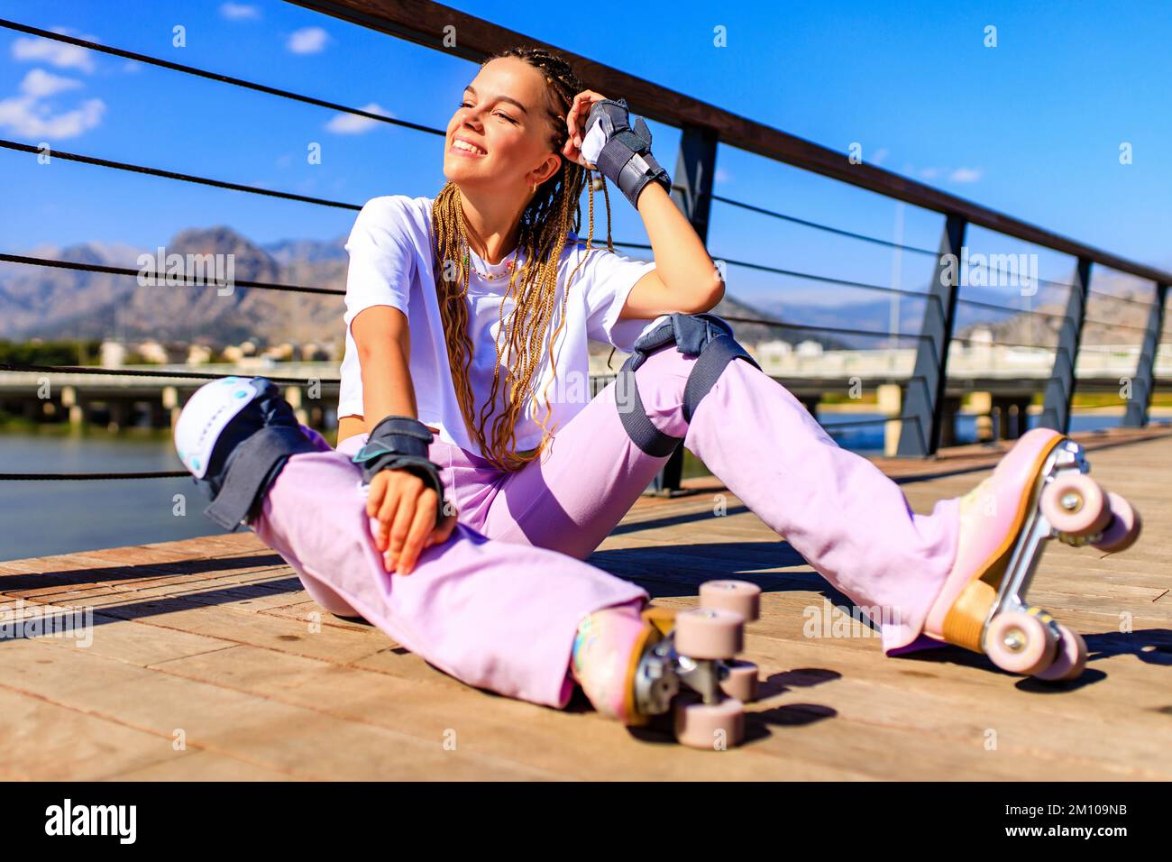 Photo of cheerful young happy woman wear white t-shirt and bell-bottomed trousers with pink pastel color roller skates outdoors in sunny day Stock Photo