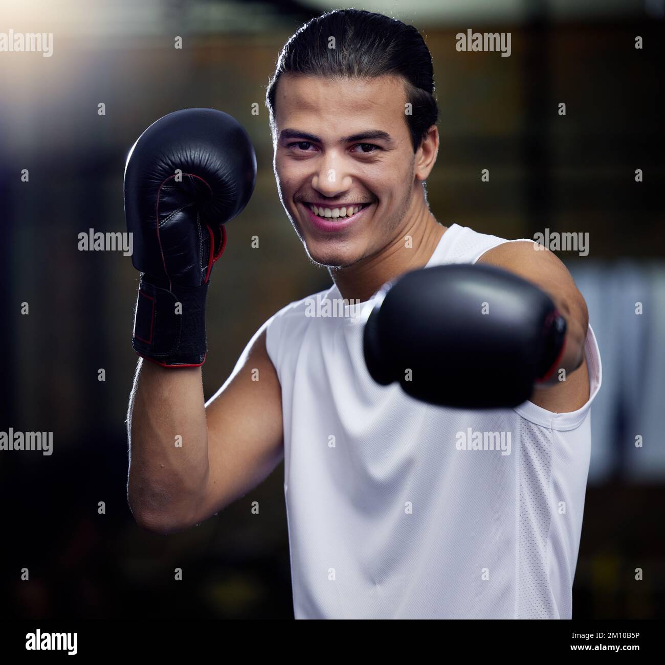 Portrait, fitness and boxing man punching with boxing gloves in a sport gym for health. Athlete, boxer and face of strong male personal trainer Stock Photo