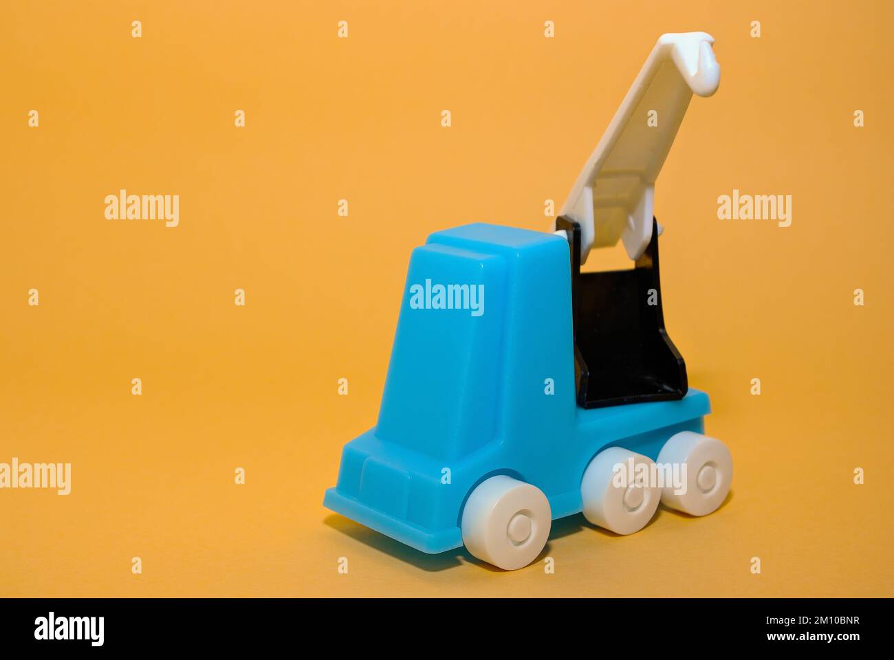 In front of a beige background, a car crane, crane truck, crane vehicle, mobile crane, plastic toy for toddlers, from the GDR of the 1980s. Stock Photo