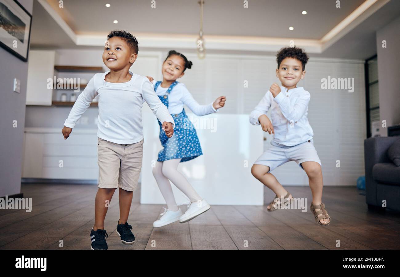 Three mixed race young children dancing and having fun in the living room at home. Siblings, two brothers and a sister, having a dance contest in Stock Photo