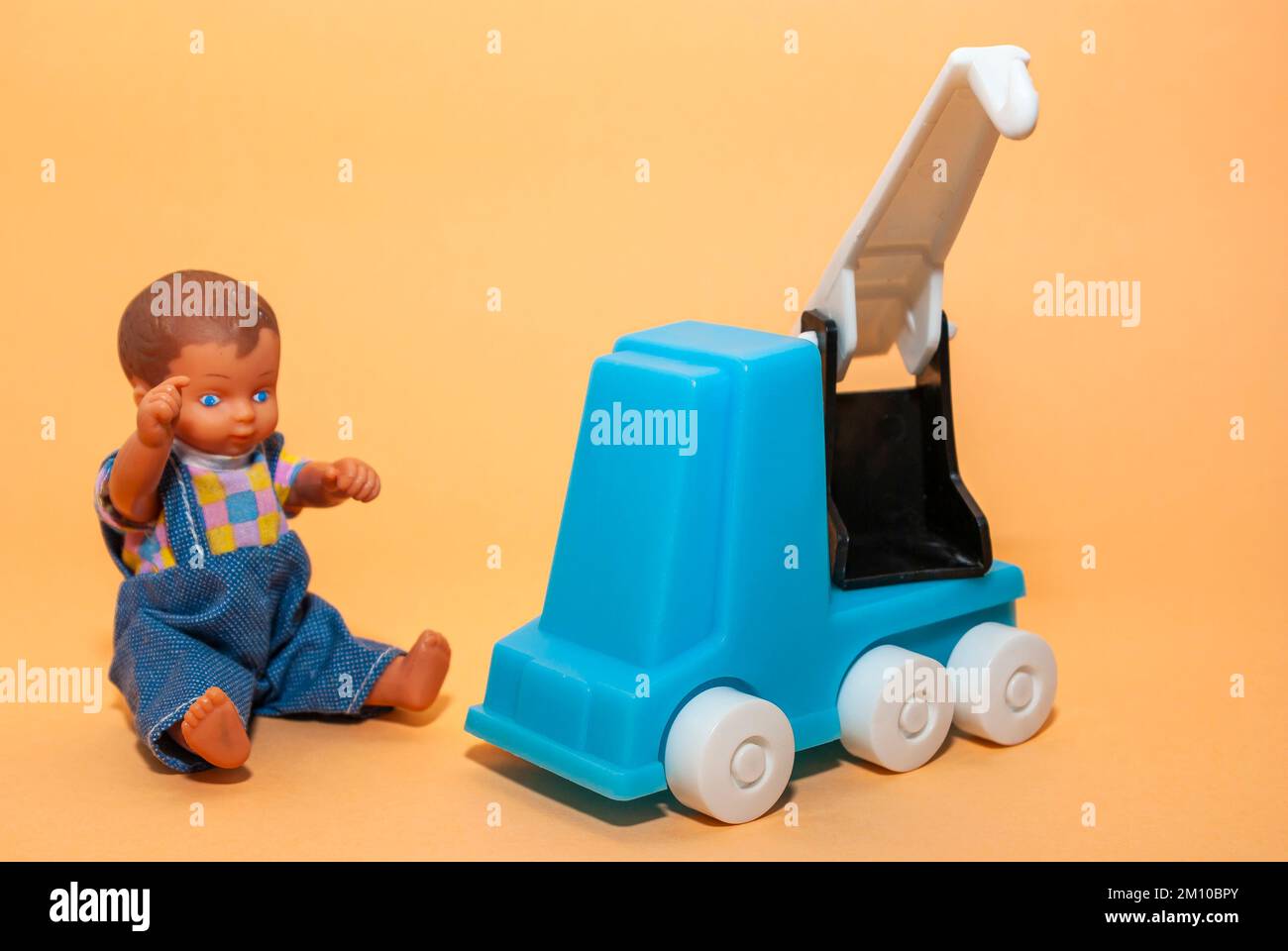 In front of a beige background, a mobile crane and a boy doll, the concept of childhood play and the construction industry. Stock Photo