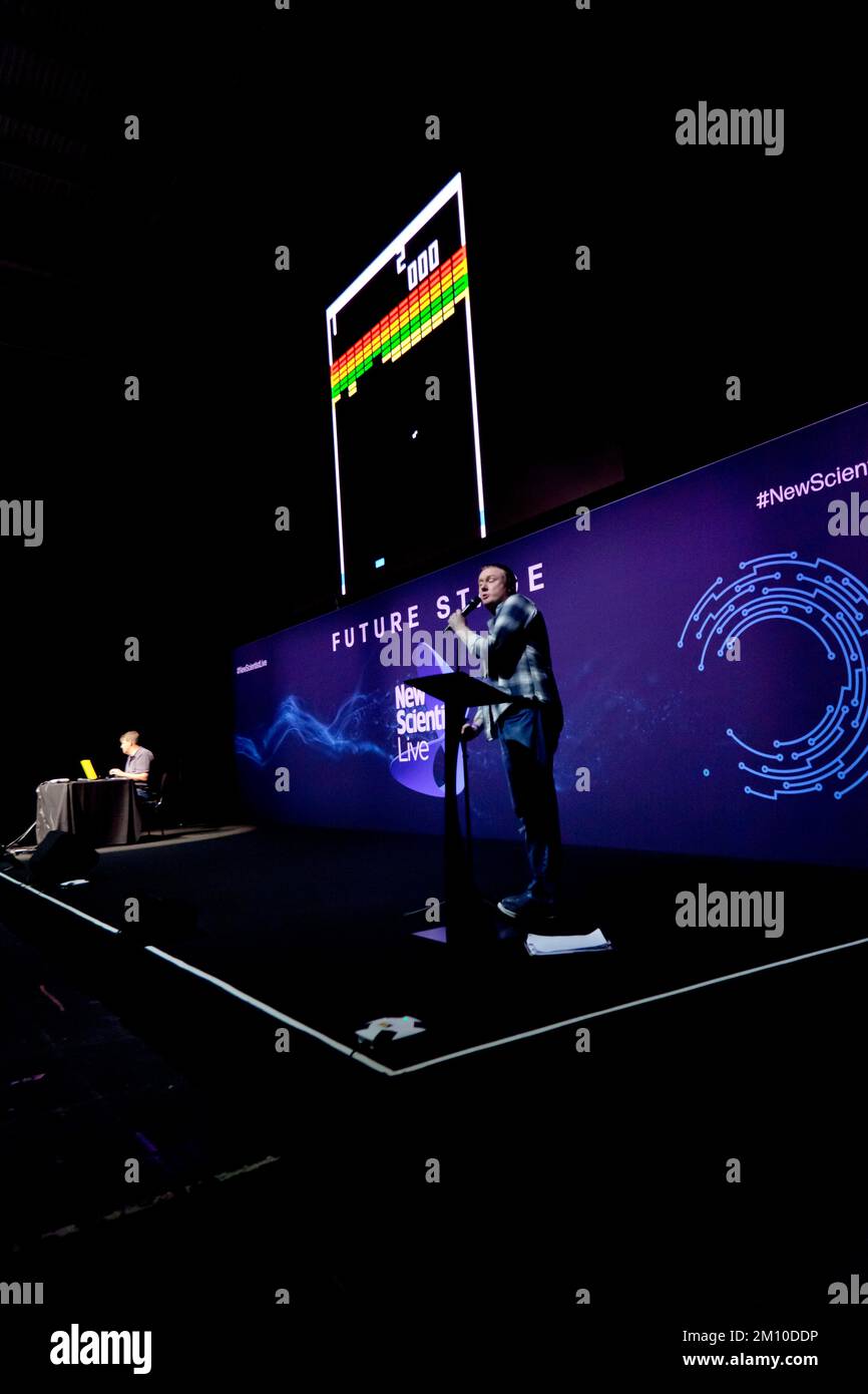 Steve McNeil assisted by Rob Sedgebeer, give a live demonstration of the  evolution of videogames, with the  audience  participating, via their  smartphones, on the Future Stage, at New Scientist Live 2022 Stock Photo
