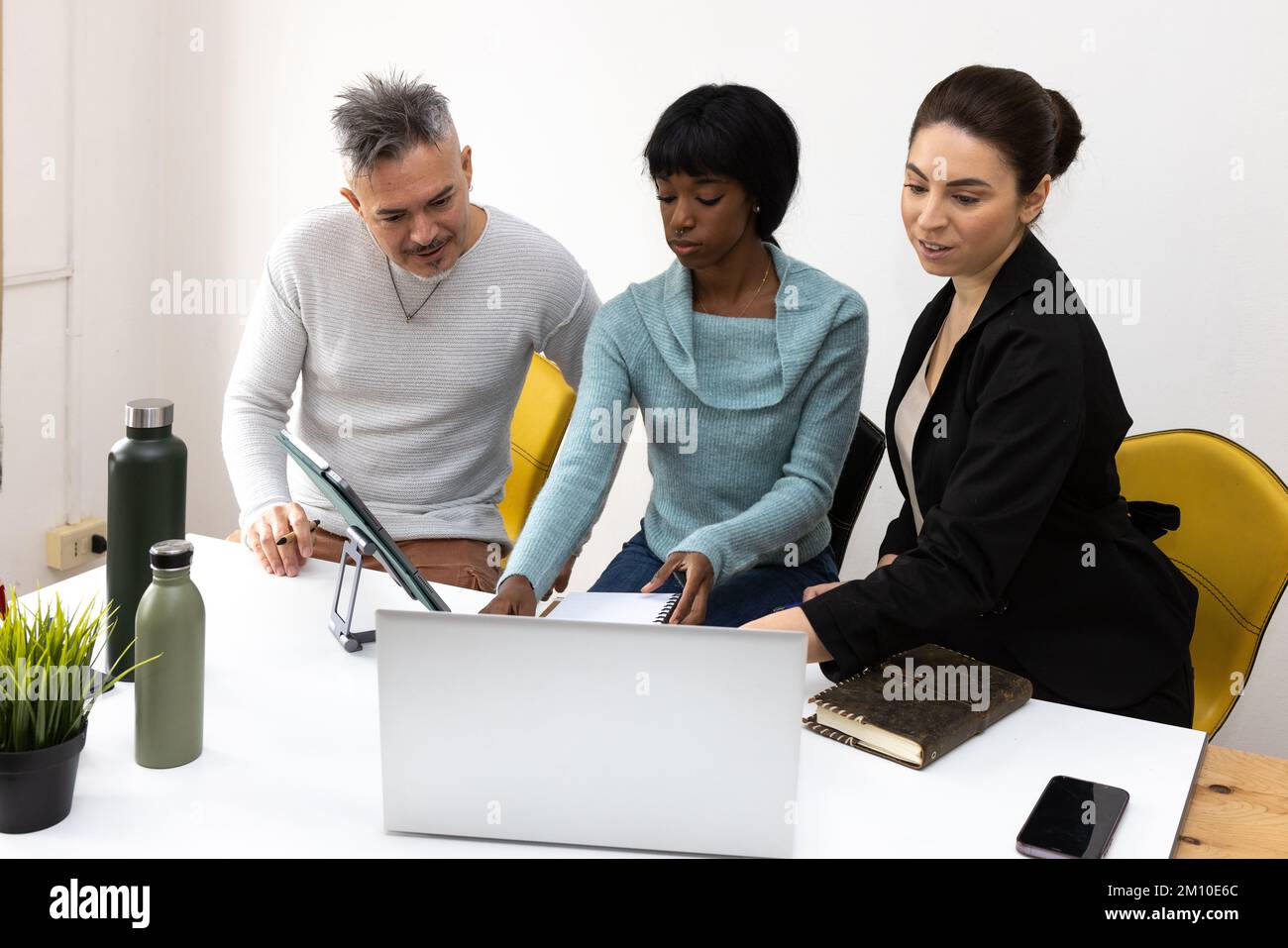 Multiethnic group of coworkers analyzing a project in the office. Desk with computer, smartphone, diaries and ecological water bottles Stock Photo