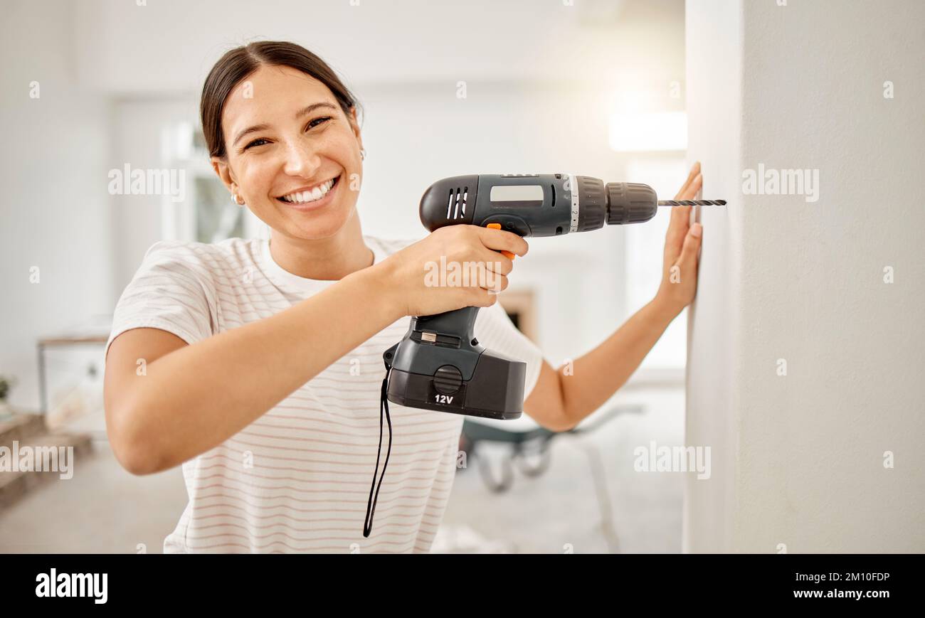 Im hanging a picture frame up here. an attractive young woman standing alone in her home and using a power drill. Stock Photo