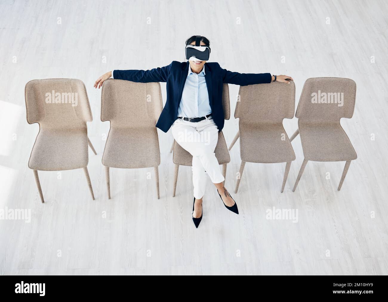 I could get used to this kind of innovation. High angle shot of a young businesswoman wearing a VR headset while sitting in line in an office. Stock Photo