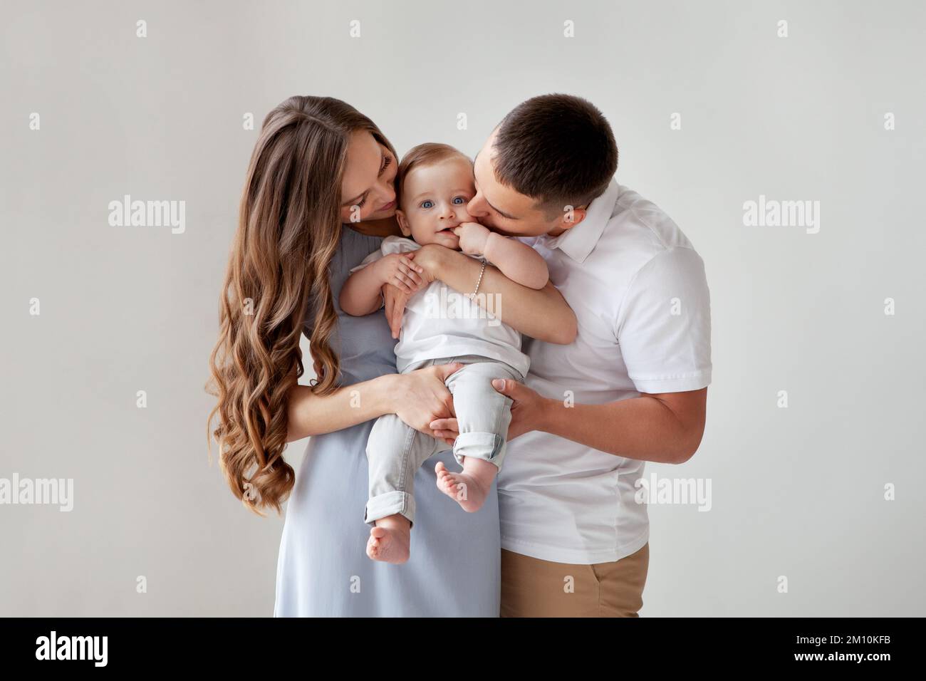 Happy young family. Beautiful Mother and father kissing their baby . Parents, Portrait of Mom, dad and smiling child on hands isolated over white back Stock Photo