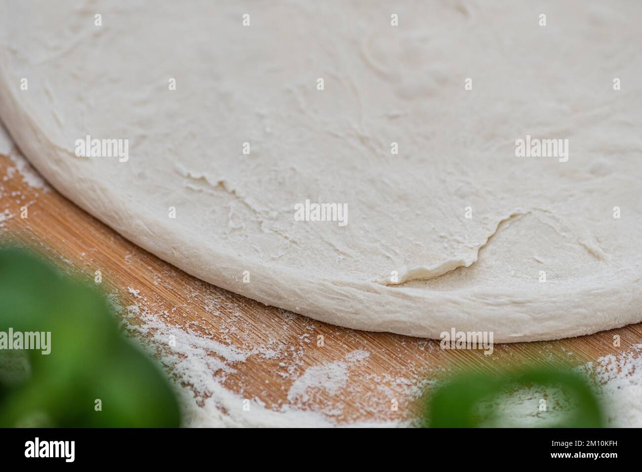 Preparing dough for pizza on a wooden board with white flour and ingredients around, close up, copy space Stock Photo