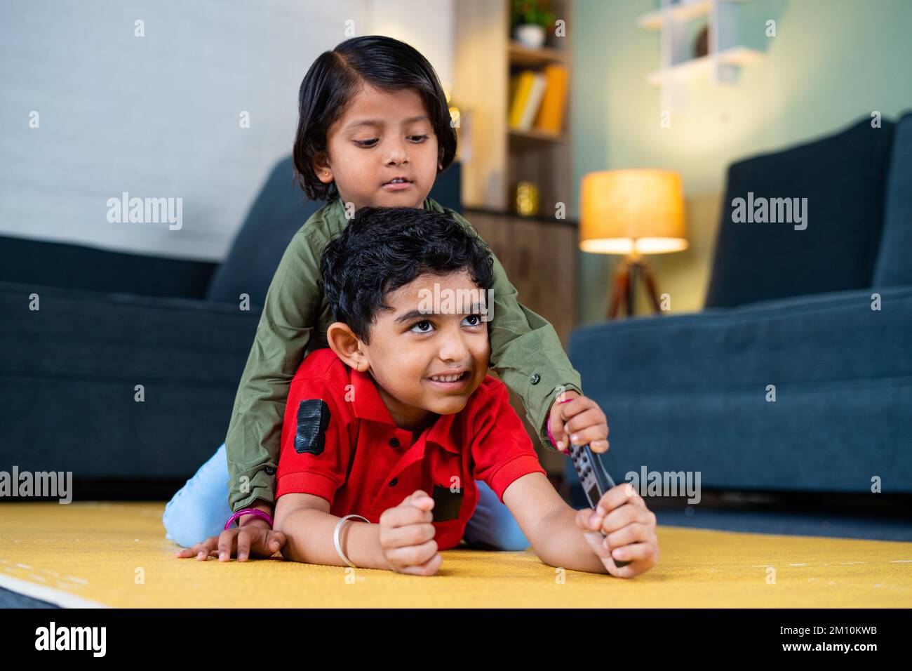 Young siblings kids fighting for remote control while watching tv or television at home - concept of childhood lifestyle, siblings quarrel and Stock Photo