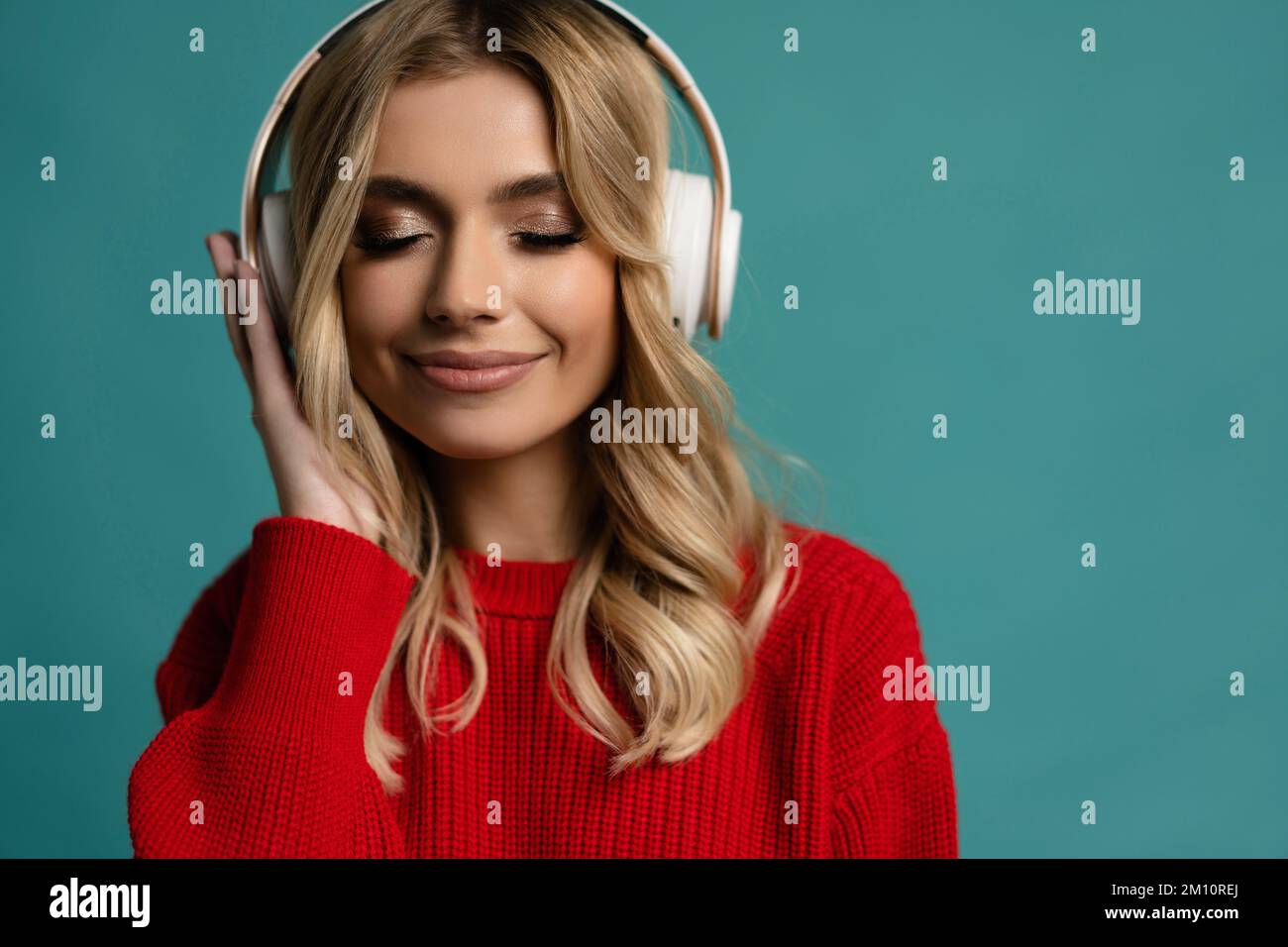 Portrait of charming blonde woman in massive headphones listening to music on isolated beige background. Stock Photo