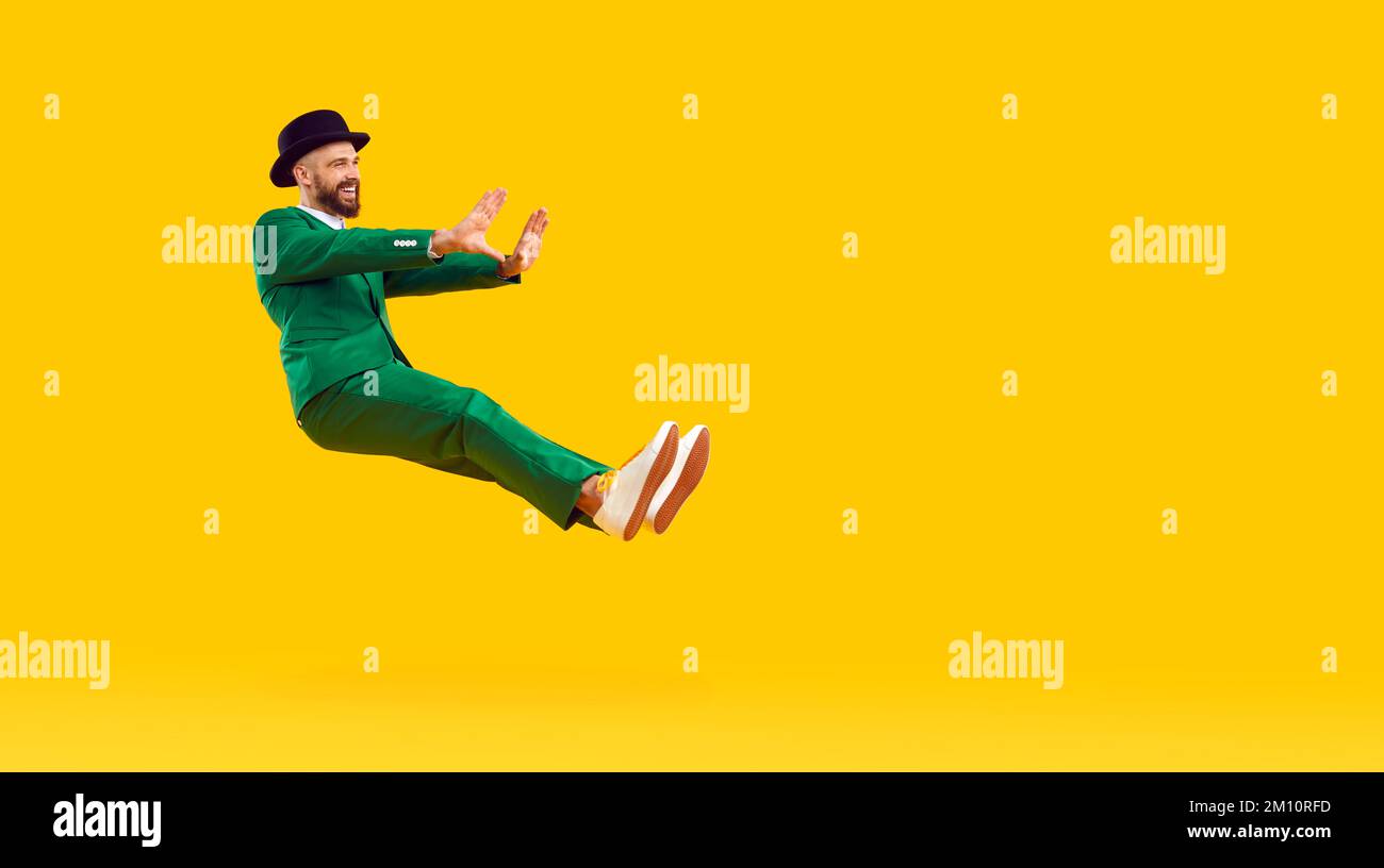 Happy man in a green suit and a black hat floating in the air on a yellow copy space background Stock Photo