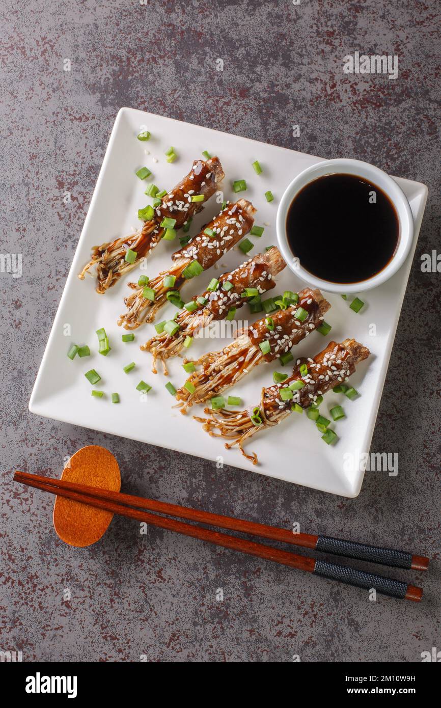 Japanese beef and enoki mushrooms rolls with teriyaki sauce close-up in a plate on the table. Vertical top view from above Stock Photo