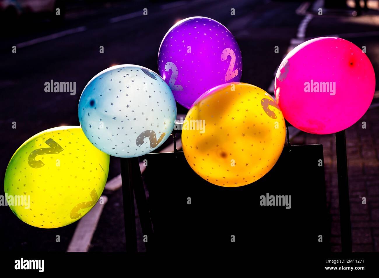 5 brightly coloured balloons in the street with a figure 2 printed on ...