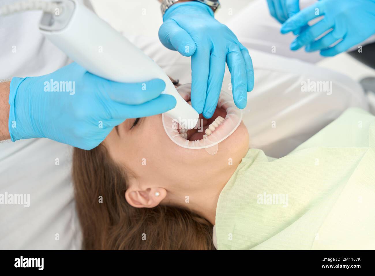Dental practitioner examining oral cavity of woman supervised by nurse
