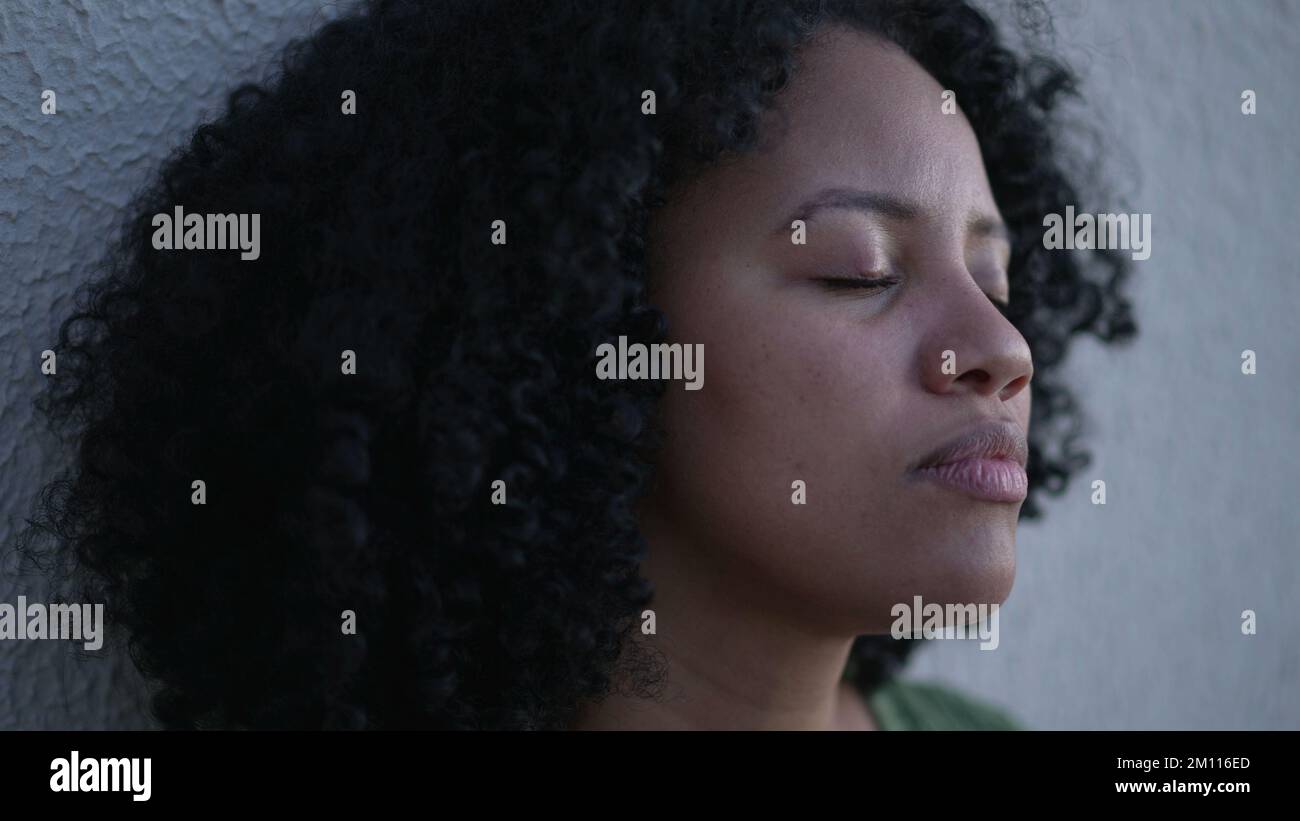 A contemplative young black latina woman closing eyes in meditation. A  pensive Brazilian adult girl opening eyes smiling Stock Photo - Alamy, image size:1300x821