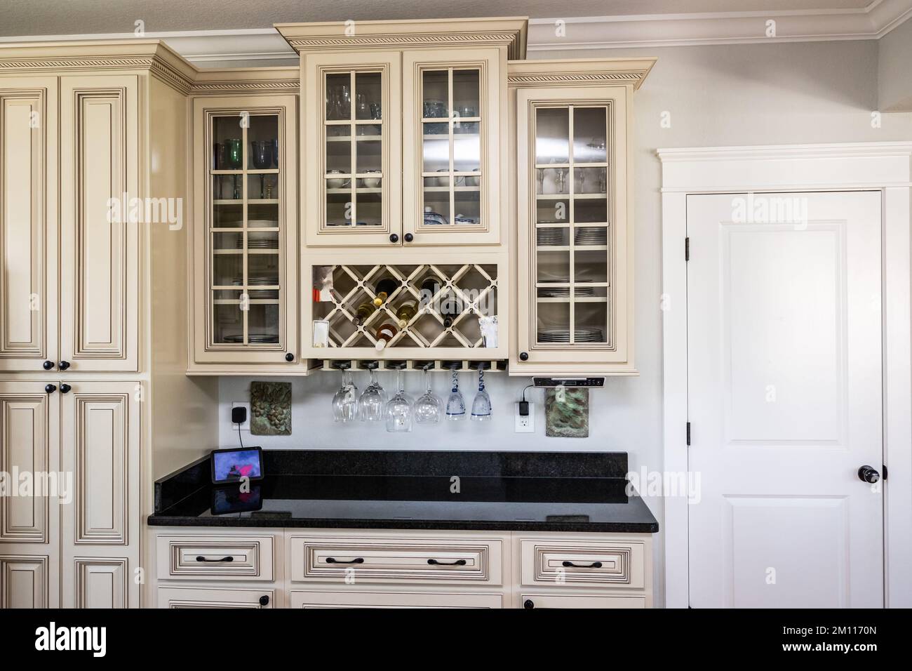 A cream colored new construction kitchen with black granite countertops clear glass cabinets and wine bottle storage Stock Photo