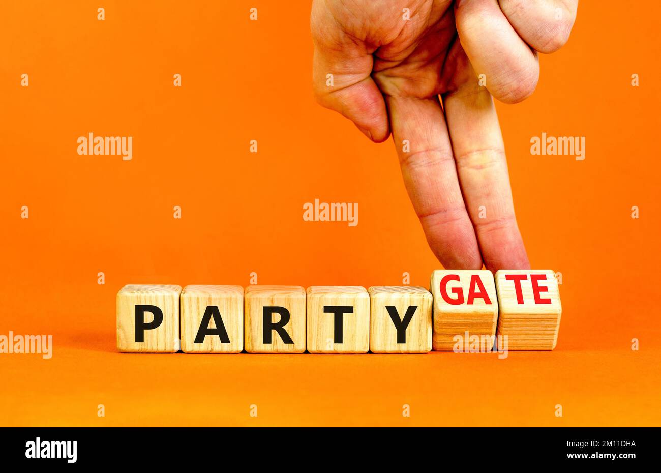 Party and partygate symbol. Concept words Party and Partygate on wooden cubes. Businessman hand. Beautiful orange table orange background. Business pa Stock Photo