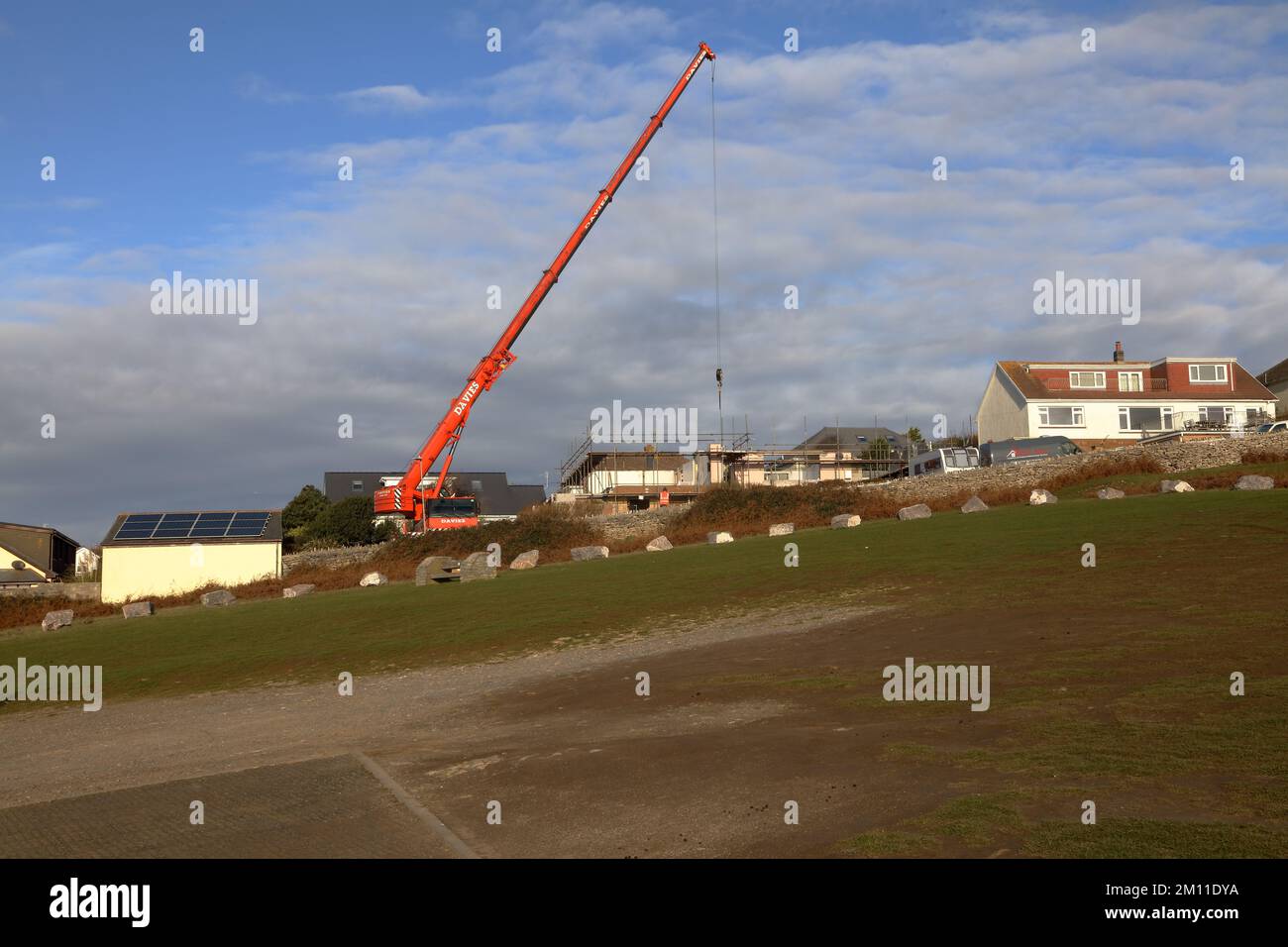 A huge Crane preparing to lift a series of steel beams into position on a house that is being rebuilt in a small village location by the sea. Stock Photo