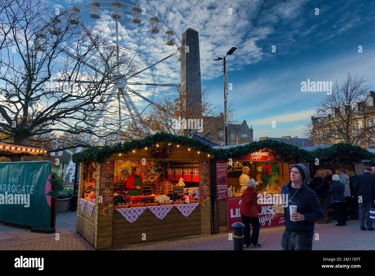 Stall holders selling food next to The Cenotaph in a pedestrian zone with a big Ferris Wheel, Harrogate, North Yorkshire, England, UK. Stock Photo