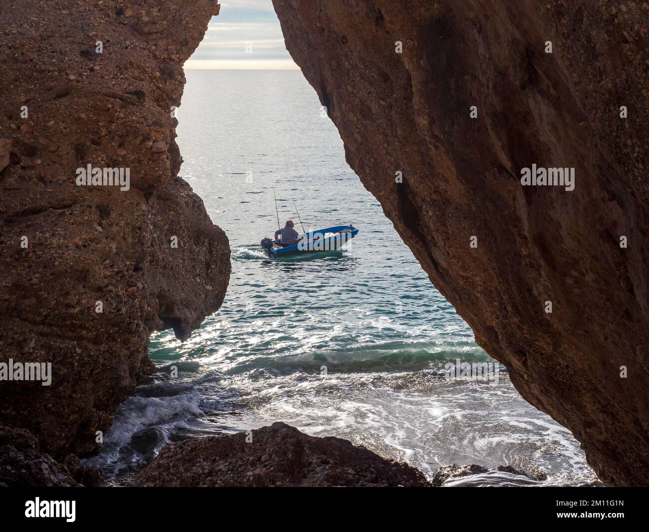 Small fishing boat sailing on the rocky coast of Nerja. Stock Photo