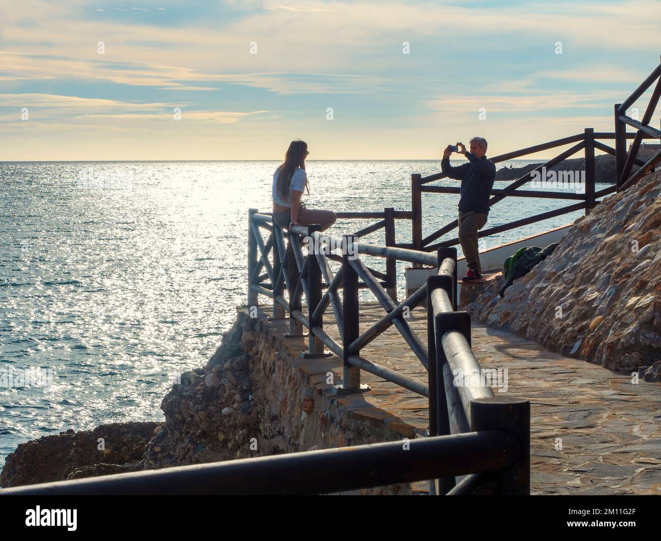 Couple taking pictures on the coastal path of Nerja at sunset. Stock Photo