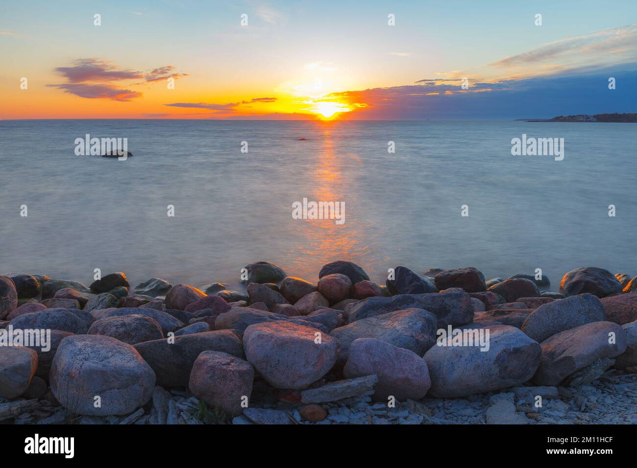 A beautiful scene of sunset sky reflecting on water with boulders of ...