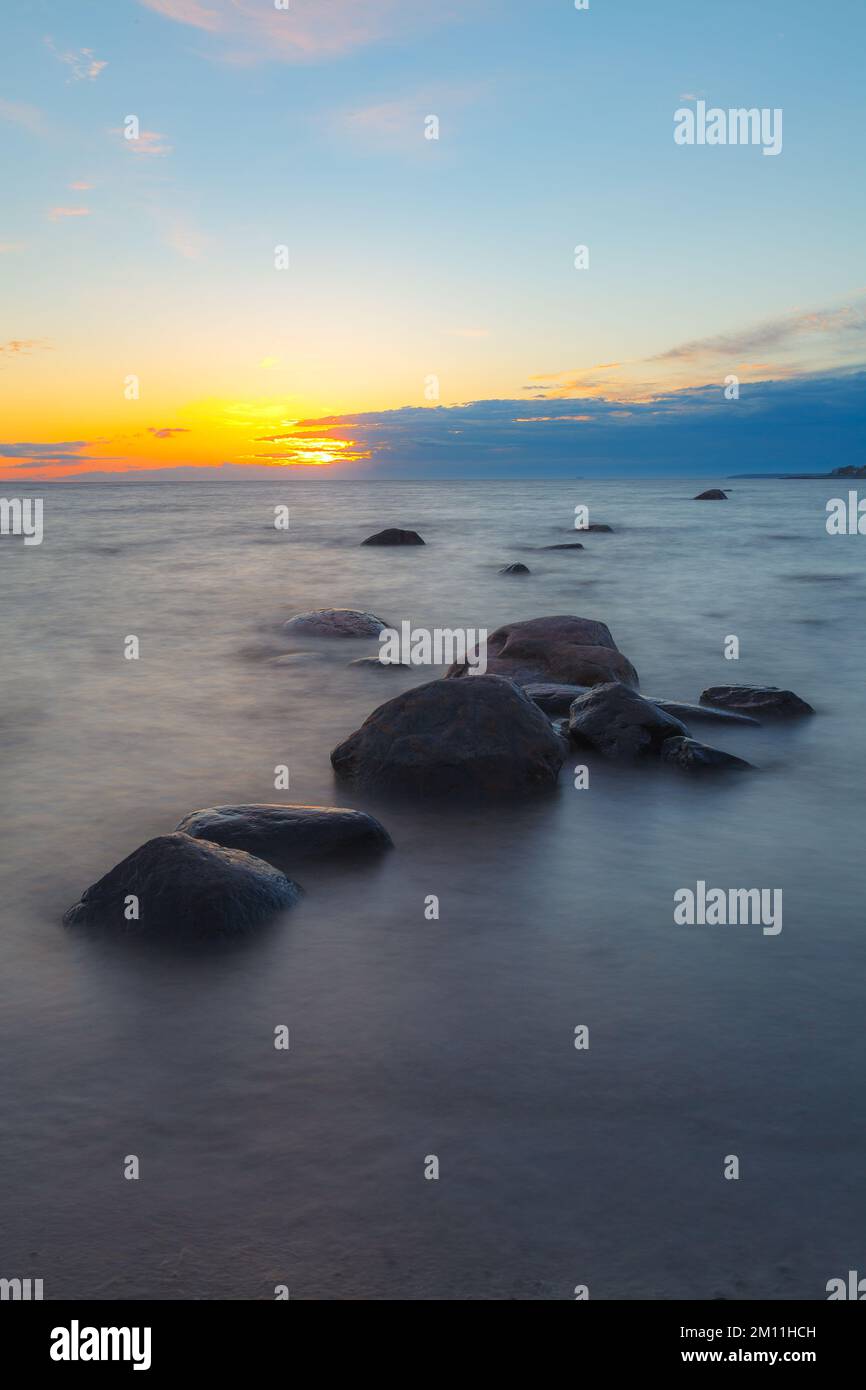 A beautiful scene of sunset sky reflecting on water with boulders of ...