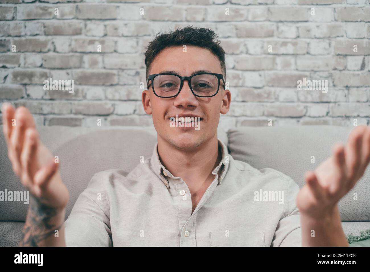 Portrait of young student talking to the camera in conference video call. Man with tattoo on his arm looking at the camera communicating for work. Stock Photo