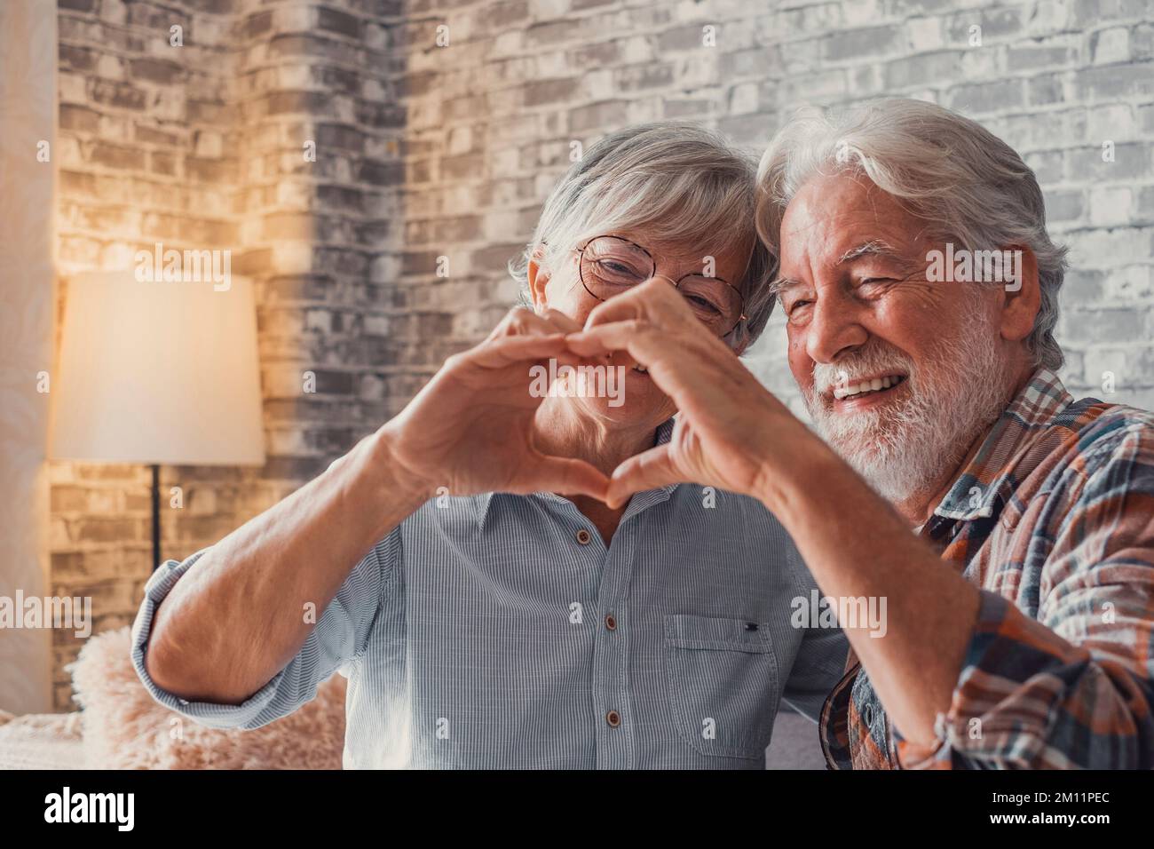Close up of hands of two mature grandparents making a heart shape with their fingers together. Smiling and having fun in love people. Stock Photo