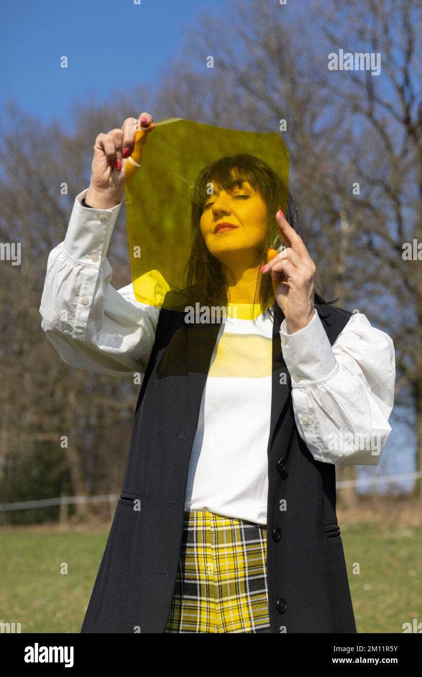 Woman looking through yellow color film, exterior shot Stock Photo