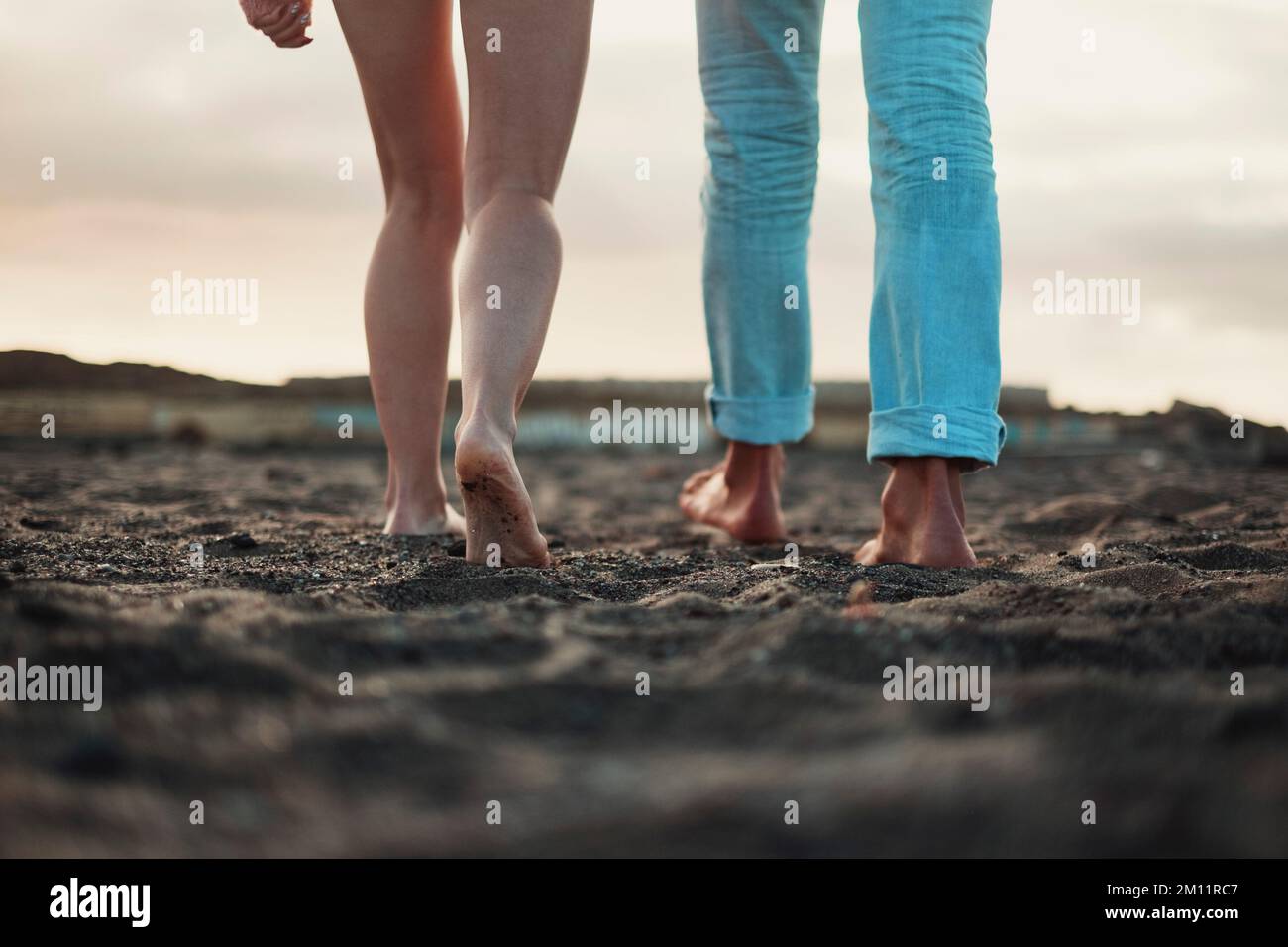 Close up and legs view for man and woman walking together on the ground in barefoot natural style. Concept of love and life together. Nudism. Couple of people walk. Sky in background. Travel. Stock Photo
