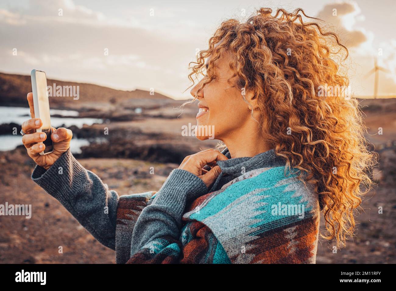 Side portrait of beautiful woman using mobile phone outdoor with internet voice connection. Modern traveler people in video call with smartphone. Leisure activity and freedom concept lifestyle Stock Photo