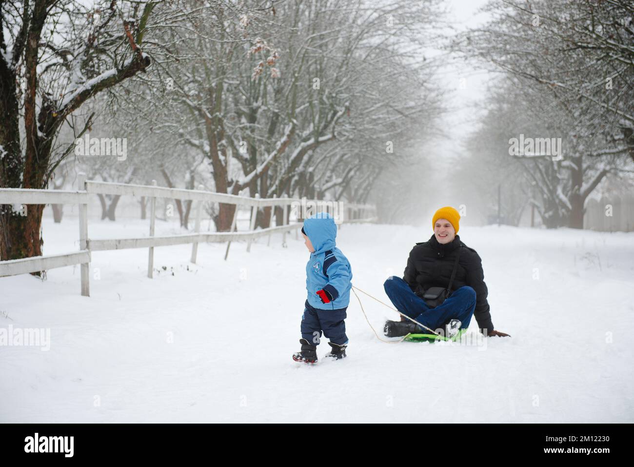 The son rides his father on a sled. Funny moments in winter. Activities in the cold season. Family spending free time together Stock Photo