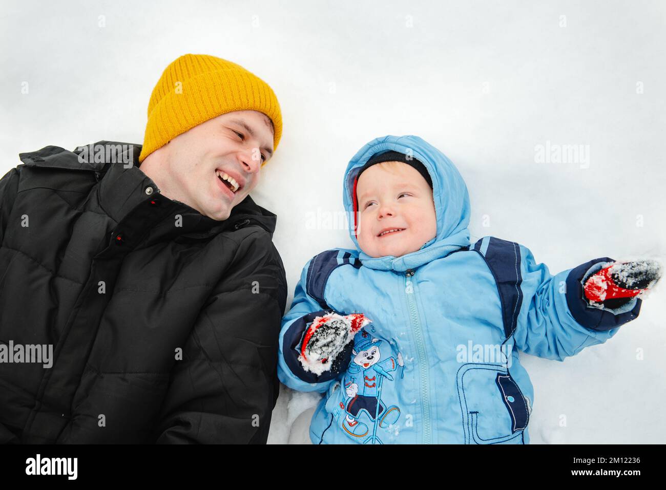 Dad and his son lie in the snow and look up. A little boy and his father playing in winter. Outdoor recreation of a family with children in winter. A Stock Photo