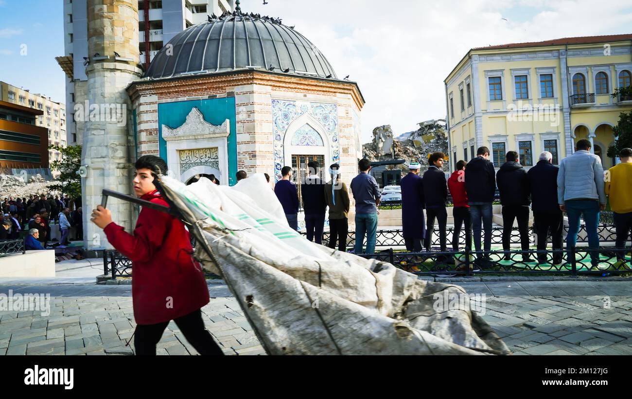 Muslims pray for Friday prayer in the garden of a historical Konak Mosque and people walk in front of this mosque in daily life of Izmir, Turkey. Stock Photo