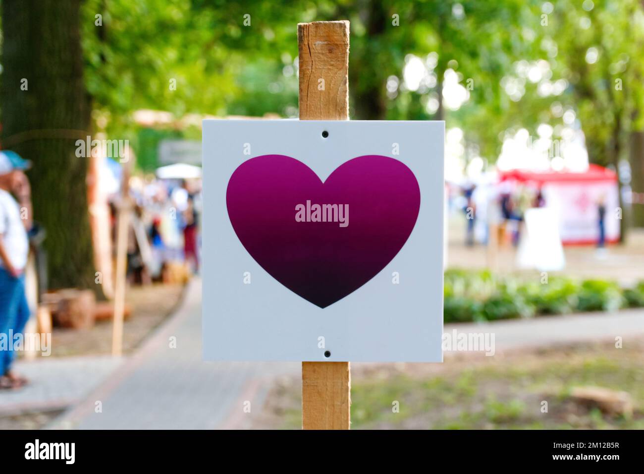Defocus white template with purple heart, advertising mock-up, banner on grass near green park festival. Love symbol concept. Information board on Stock Photo