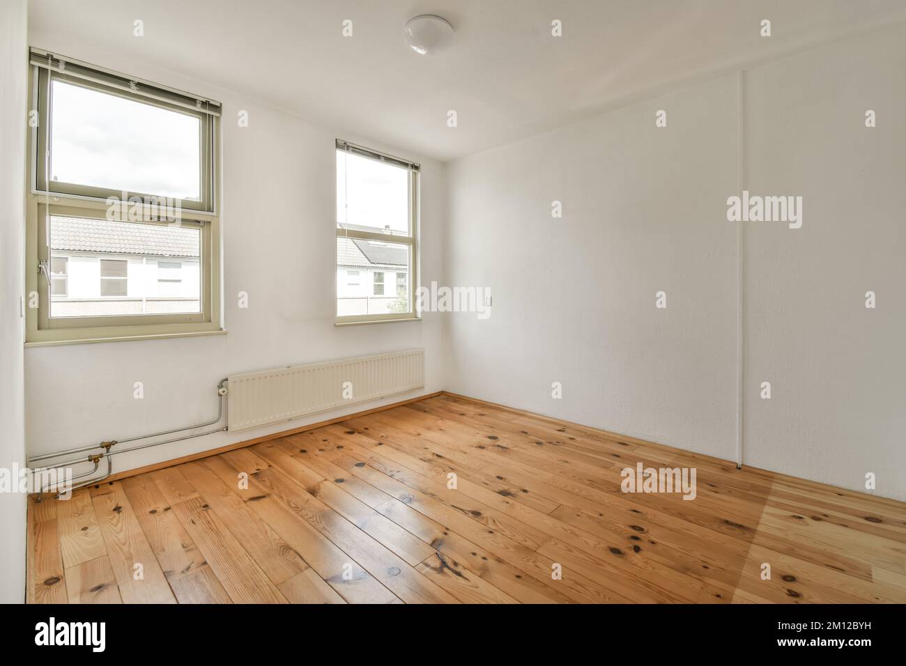 an empty room with wood flooring and white paint on the walls, there is a window in the corner Stock Photo