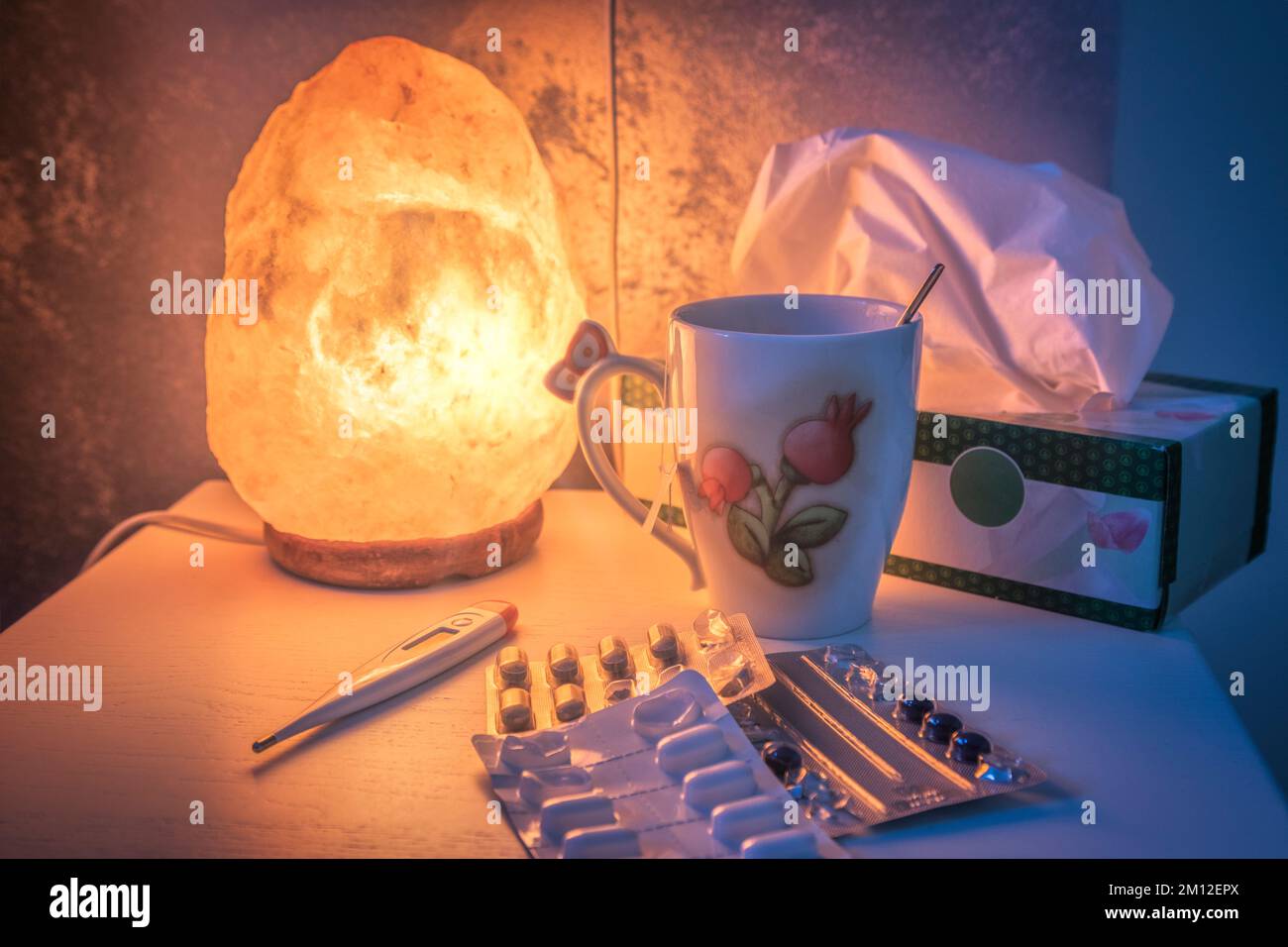 bedside table lighted by a salt lamp, with medicines and fever thermometer Stock Photo