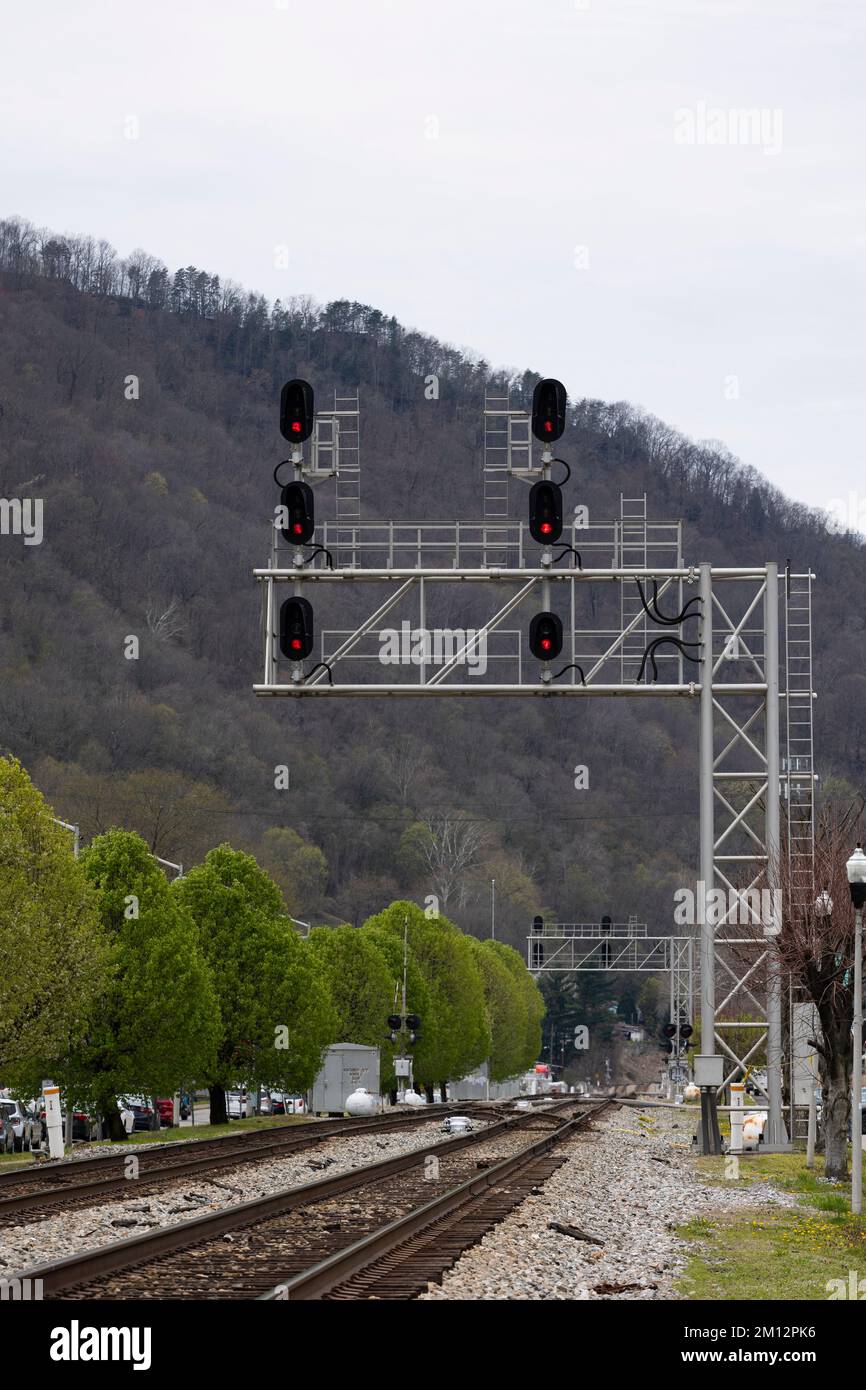 A large metal cantilever style railroad signal bridge structure hangs over two main train tracks in a small town in the Appalachian Mountains in WV. Stock Photo