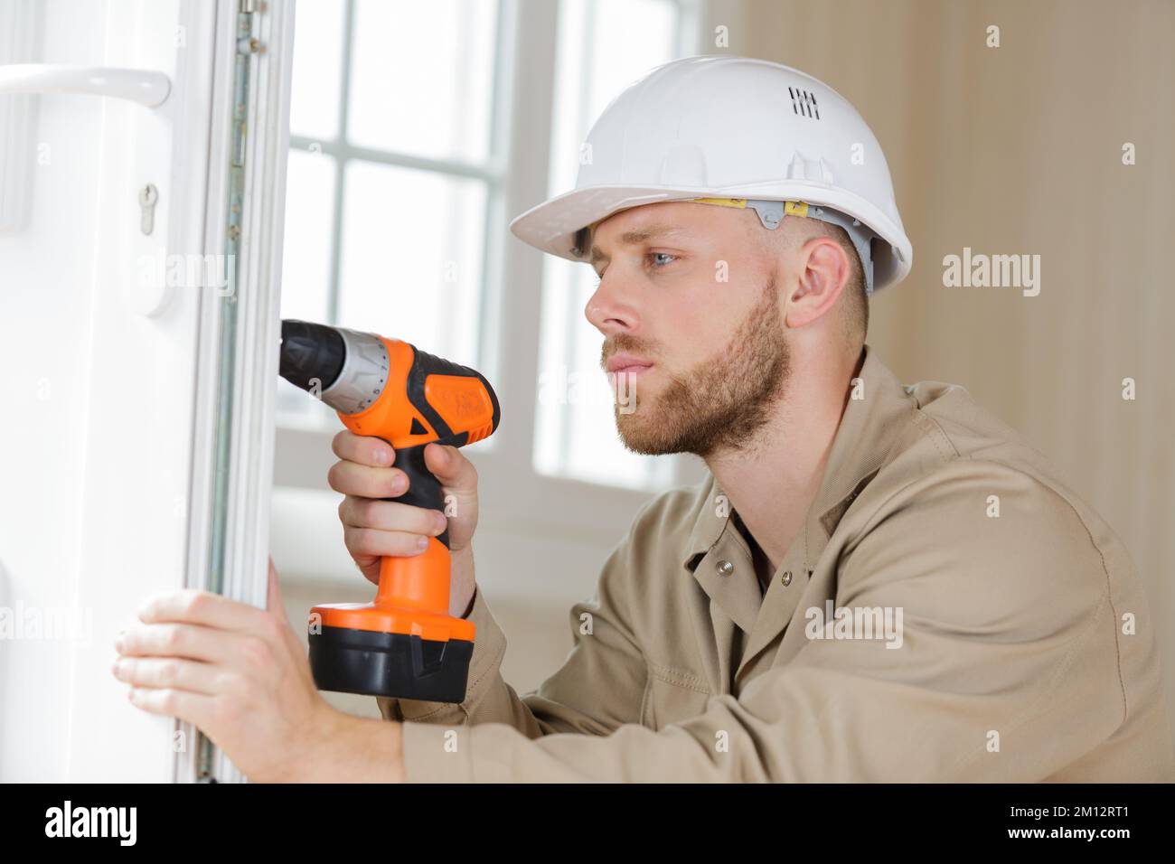 young contractor using cordless drill on door lock Stock Photo