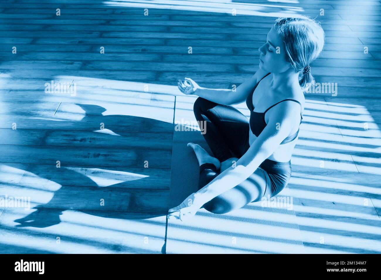 Young woman meditating sitting in lotus position against sunny window ...