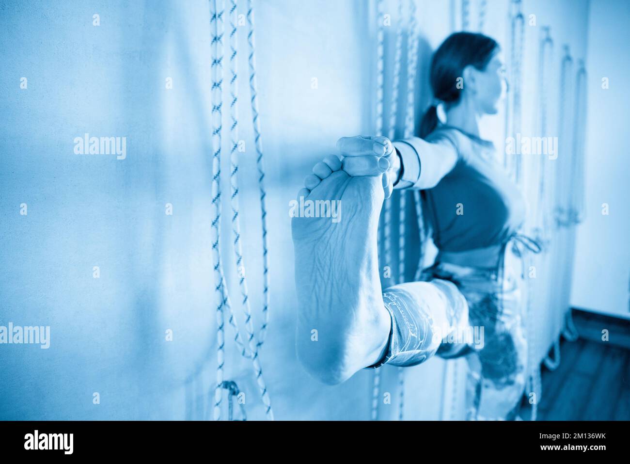People Using Toe Rope Young girl doing yoga pose holding her toe standing against wall with ...