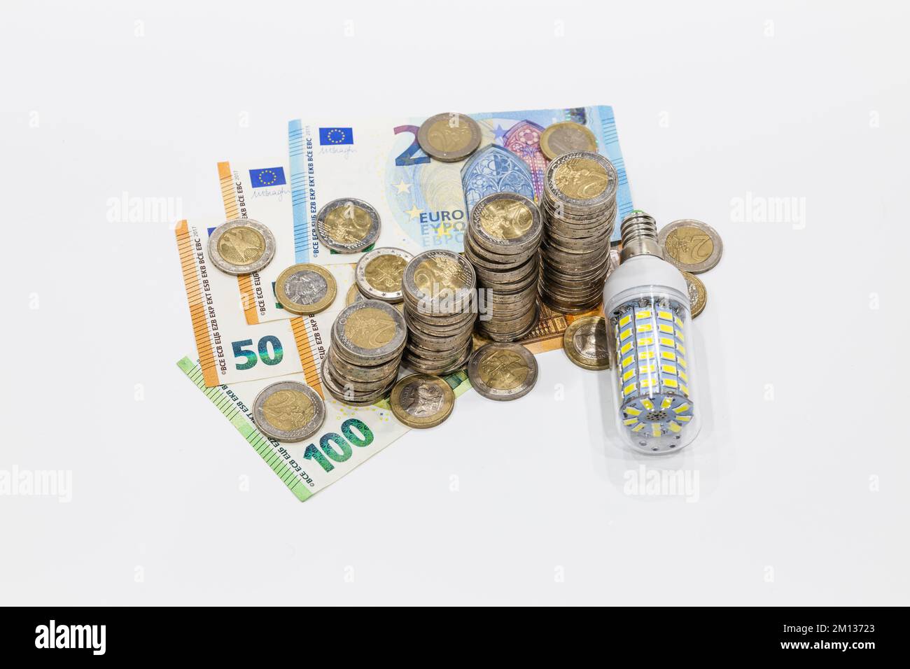Stacked coins on Euro banknotes and light bulb. Concept of expensive electricity costs Stock Photo