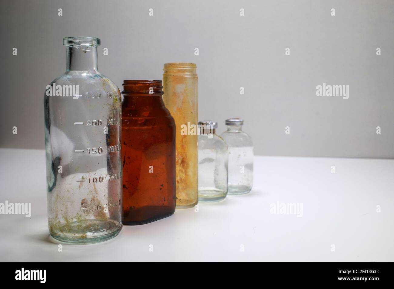 One medical beaker,  one amber glass medical pill bottle, One glass test tube, and  two clear glass vaccine bottles on a white background Stock Photo