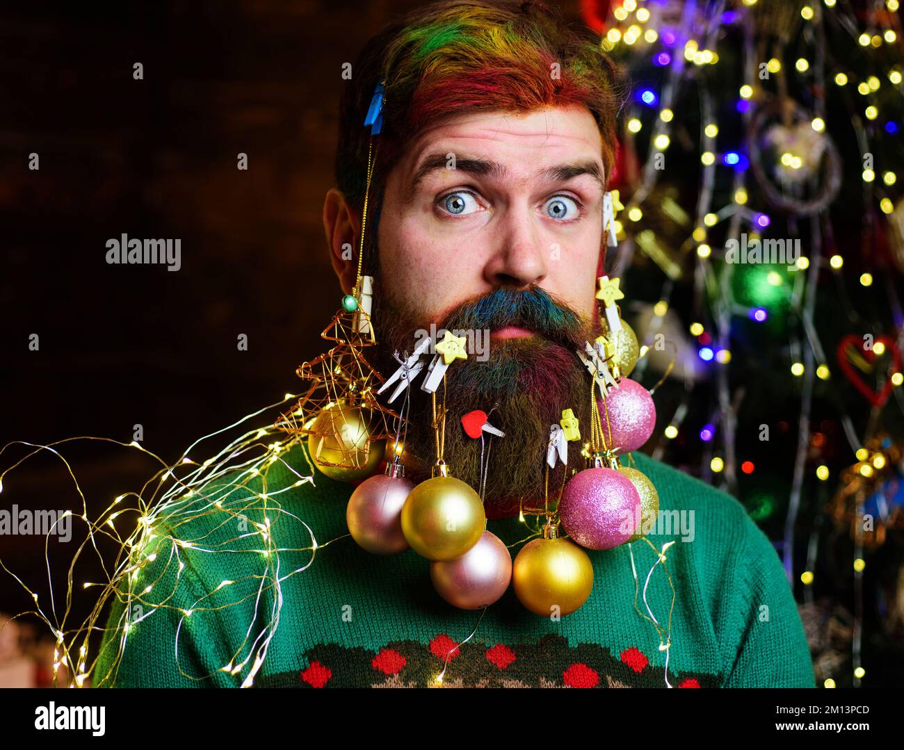 New year party. Surprised bearded man with Christmas beard decorations and dyed hair Stock Photo