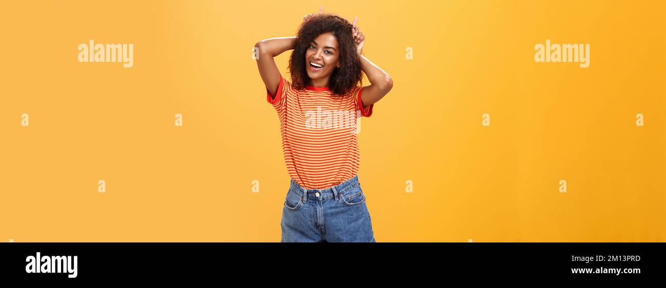 Rebellious playful and joyful african american girl with curly hairstyle making devil horns on