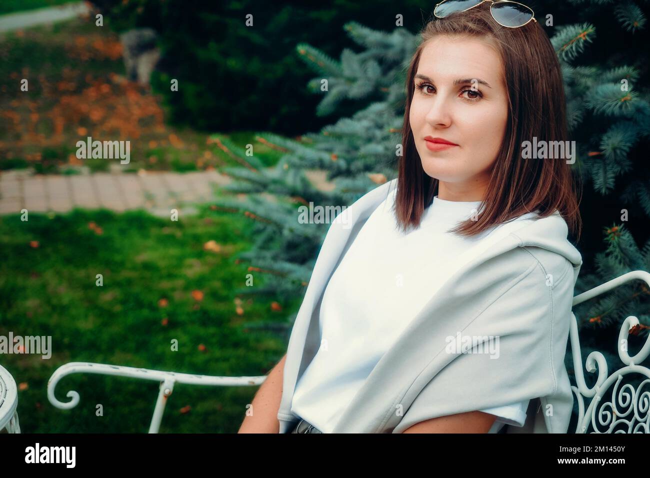 Beautiful Caucasian woman sits on park bench and looks away. Portrait of girl 30 years old.. Stock Photo