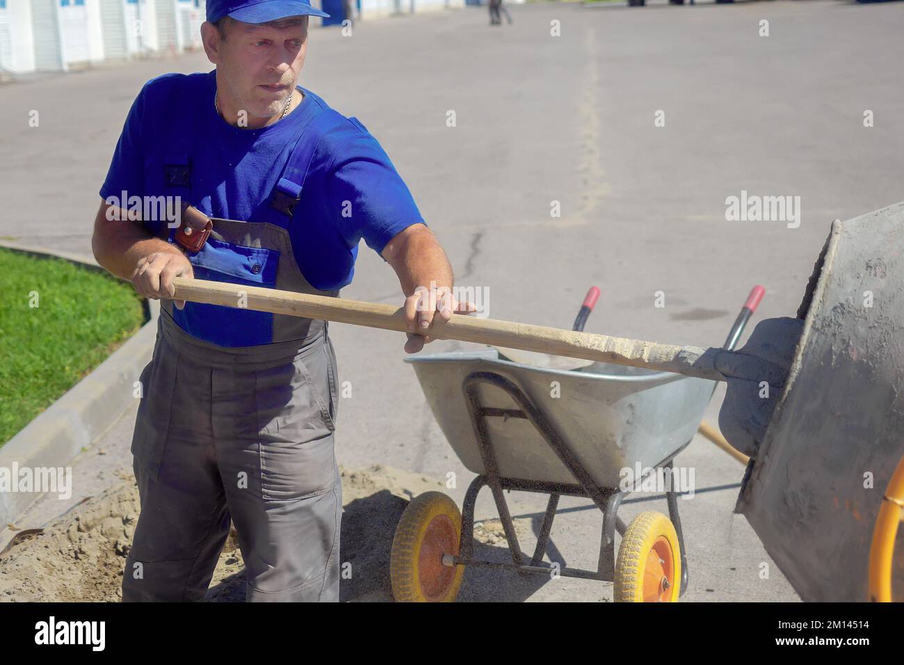 Builder with shovel interferes with cement mortar for construction. Elderly working man works on construction site on summer day.. Stock Photo