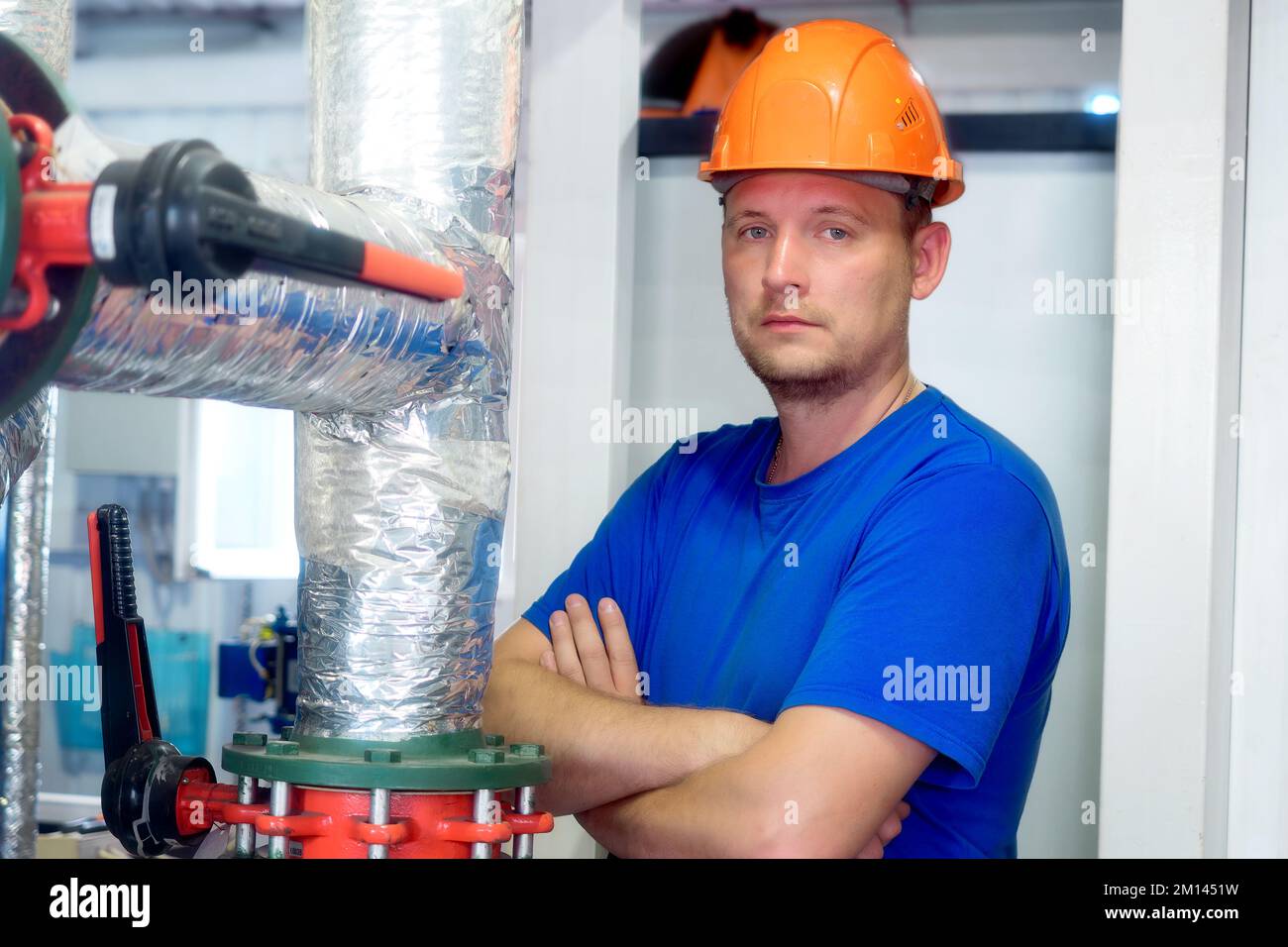 Portrait of engineer in construction helmet and work clothes on industrial background inside premises. Gas industry worker inside boiler room. Beginning of heating season in Europe.. Stock Photo