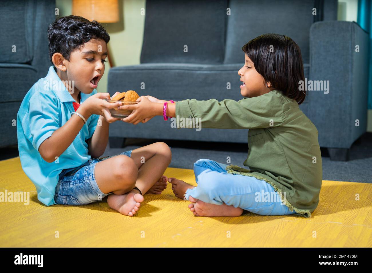 Young siblings kids fighting for snacks or biscuit while sitting on floor at home - concept of childhood lifestyle, relationships and weekend holidays Stock Photo
